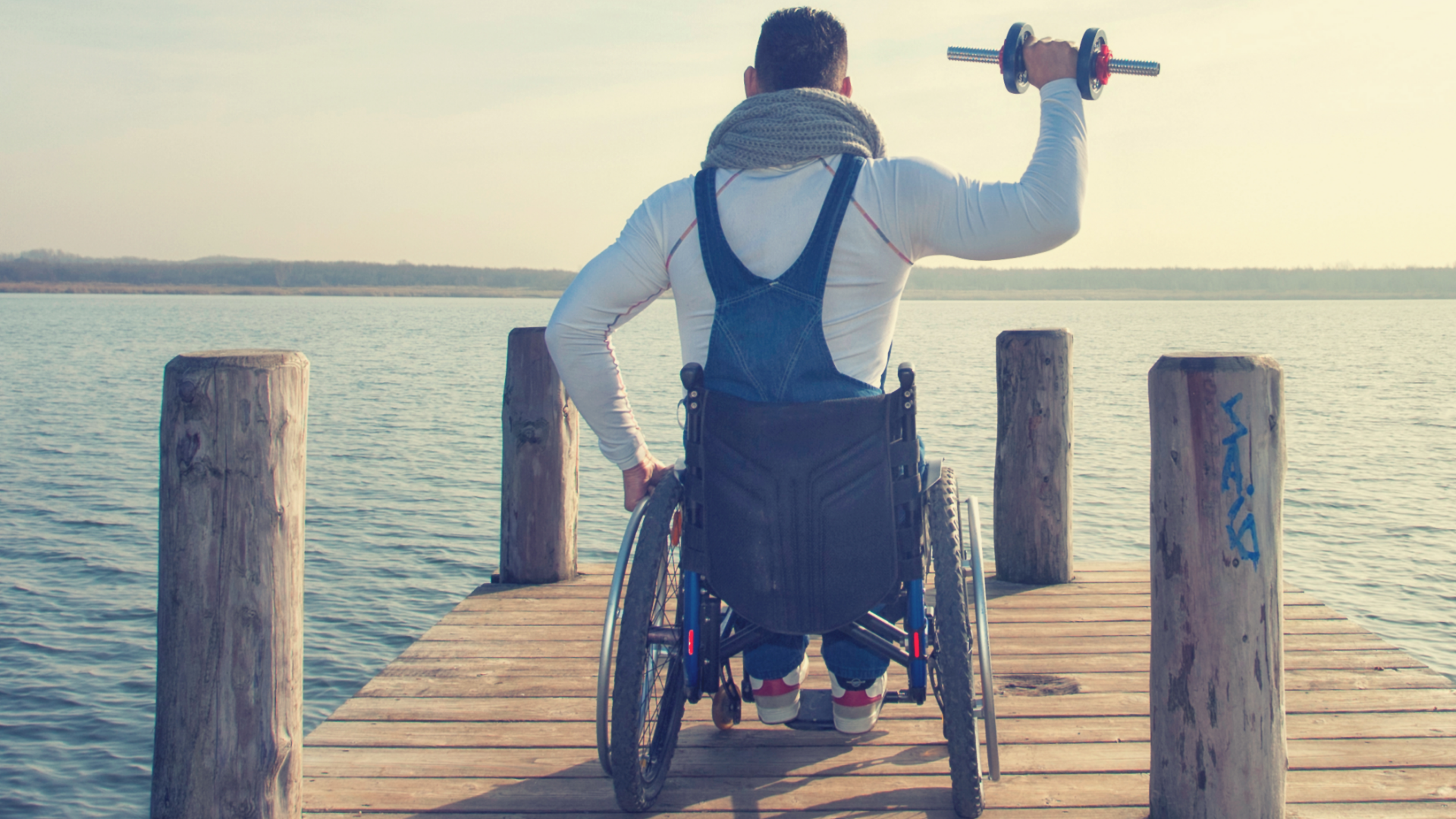 man in wheelchair with back turned holding up a dumbell on a dock