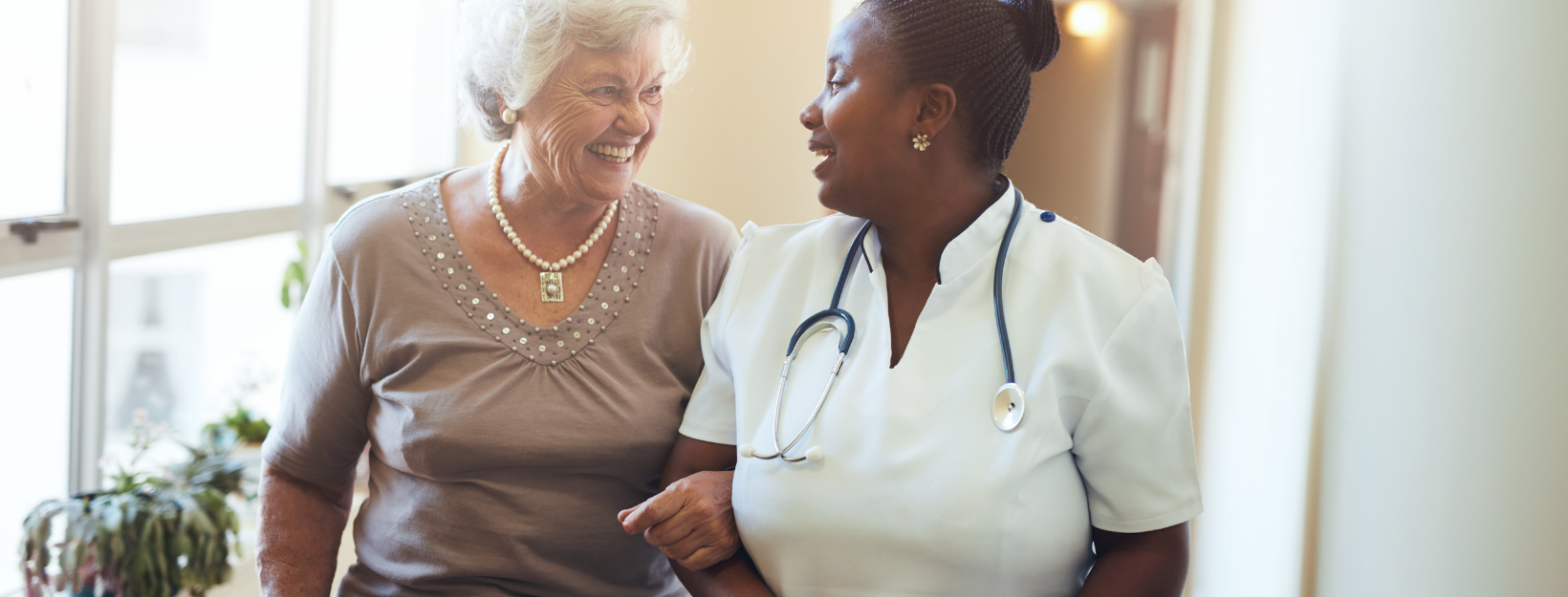 eldefrly woman and nurse linkin arms while smiling at one another