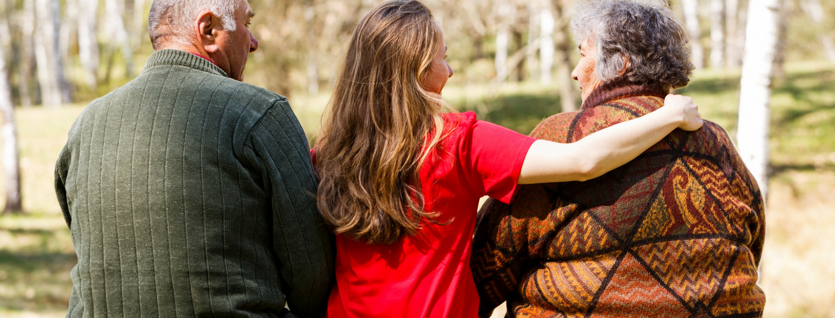 three people with their backs turned sitting on a park bench toung lady has her arm aroynd an elderly woman an older man is to the young womans left