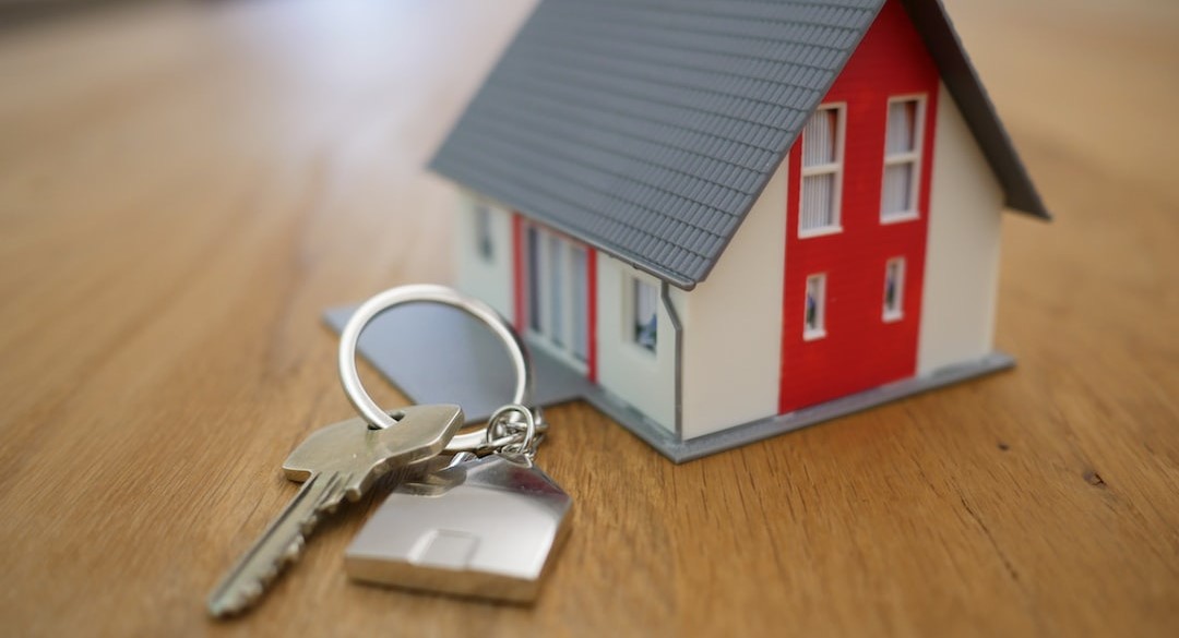 Financial Literacy Mortgage Key on a house shaped keychain, on a table next to a miniature doll house.