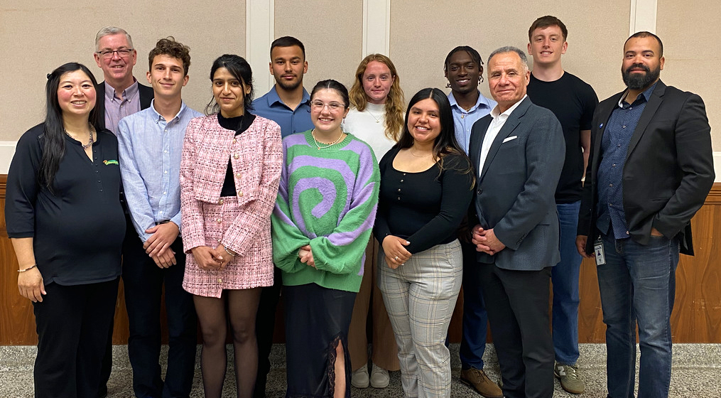 A group photo with 12 people, including 8 college-aged students and Carlos Martinez.