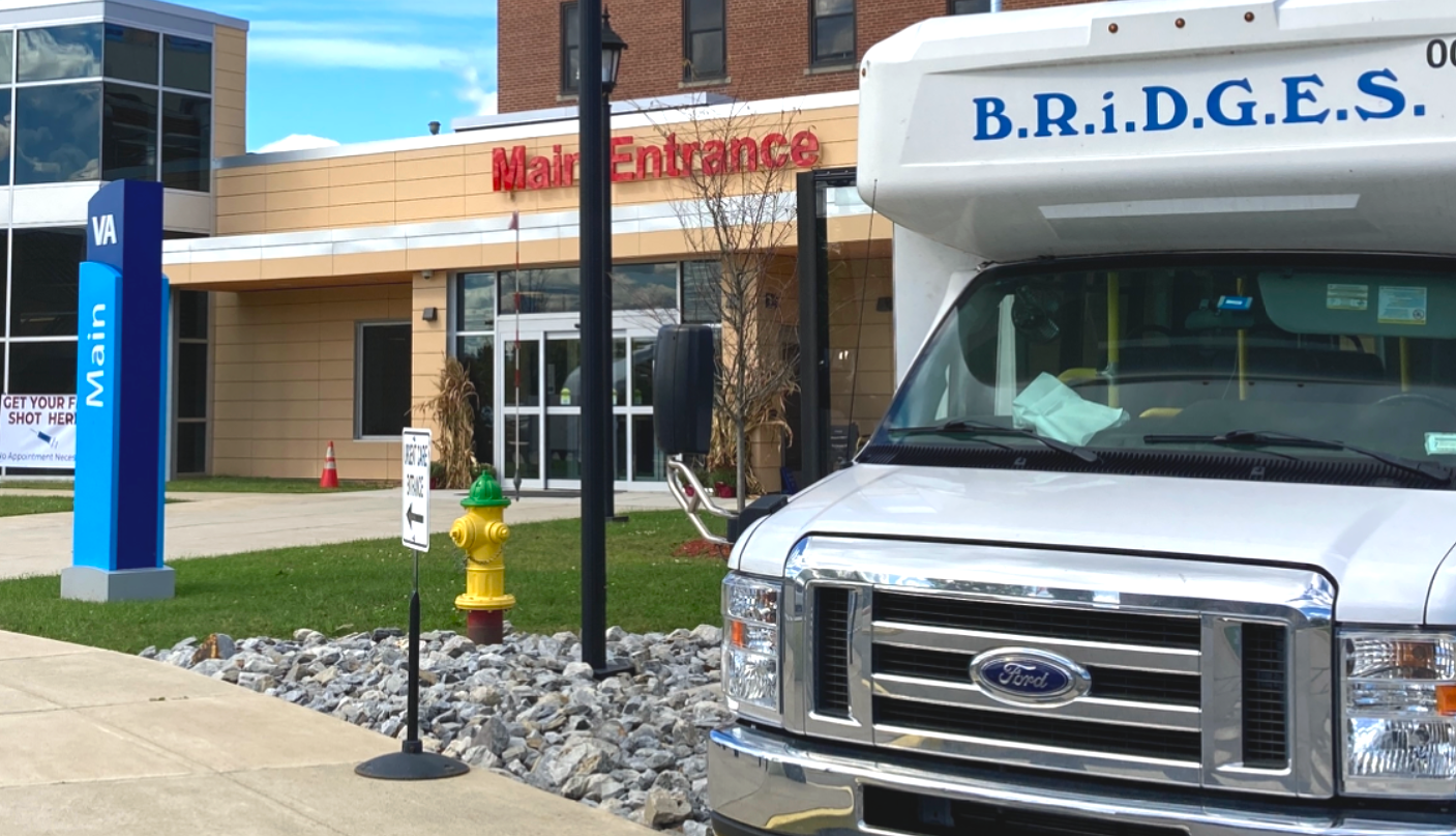 Transportation A bus with Bridges written on the front parked in front of a building. Above the door on the building says "Main Entrance."